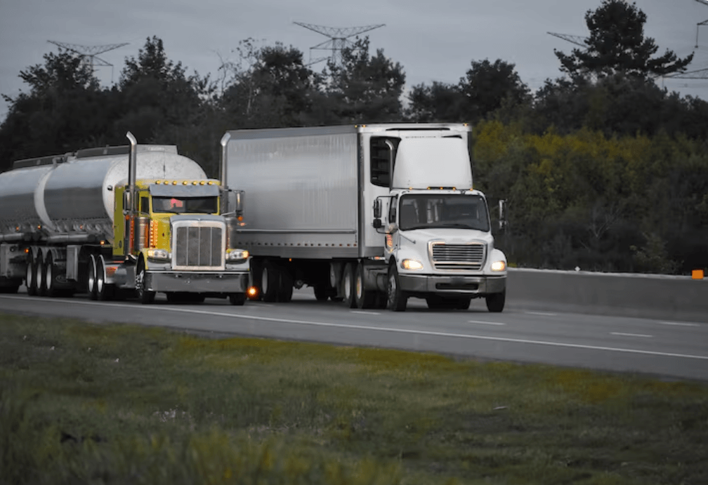 Yellow tanker truck and white semi-truck hauling freight along a multi-lane highway