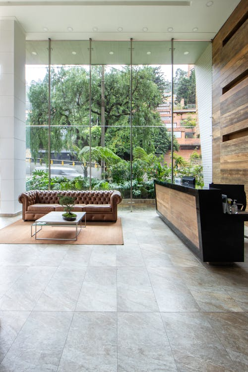 Modern boutique hotel lobby with reception desk, leather sofa seating, and large floor-to-ceiling windows overlooking greenery