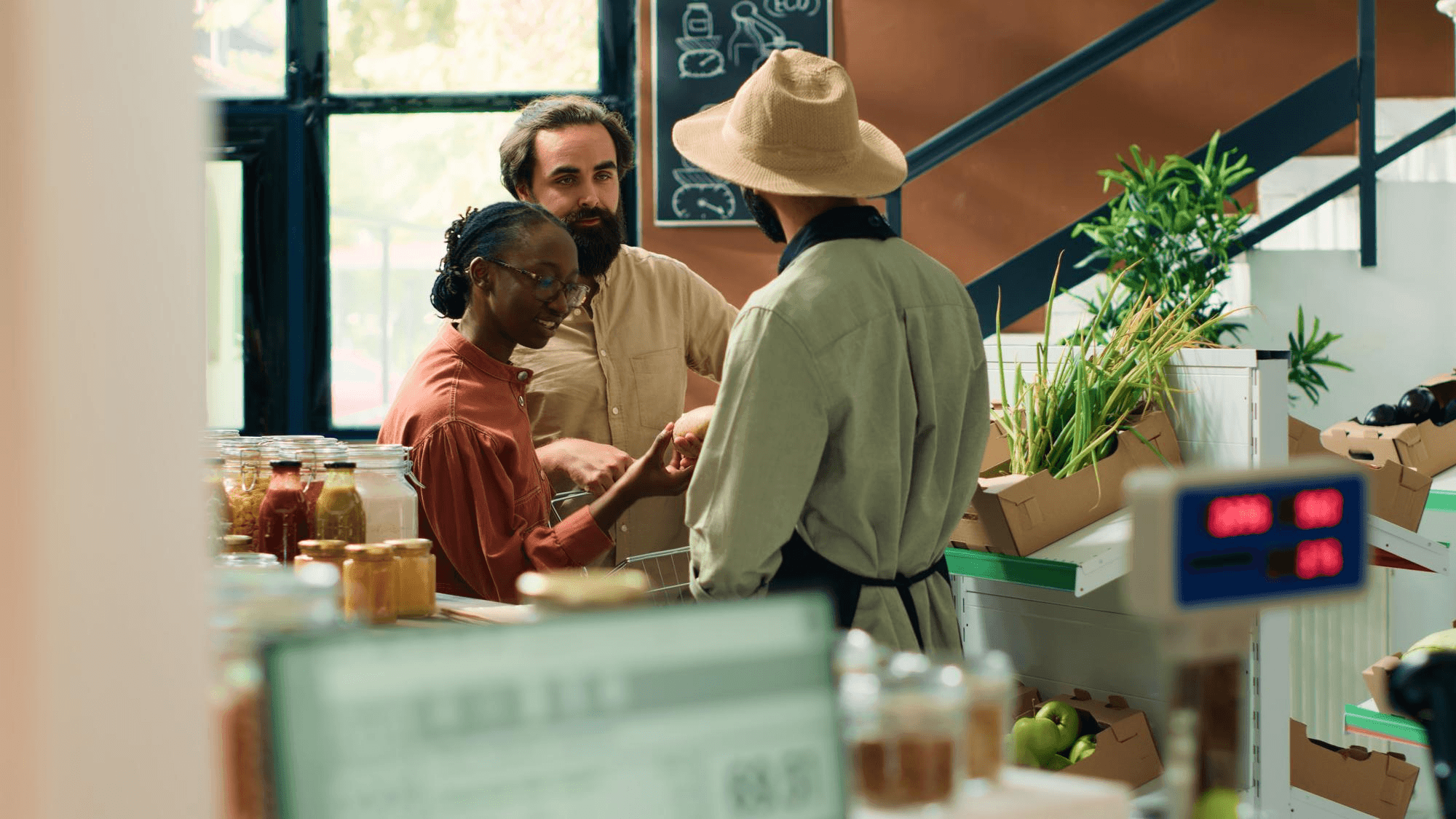 Couple speaking with a shop clerk at the counter of an organic grocery store filled with fresh produce