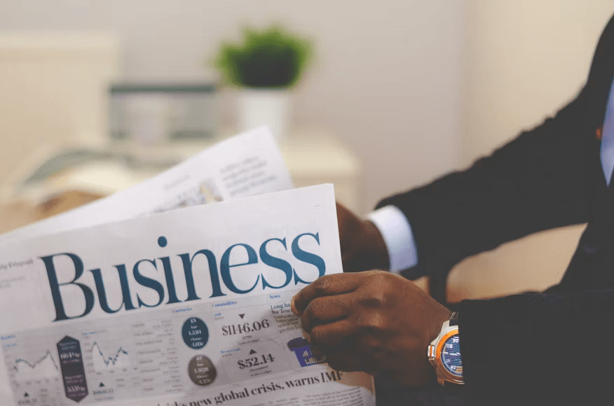 Businessman in a suit holding and reading the Business section of a financial newspaper displaying market data