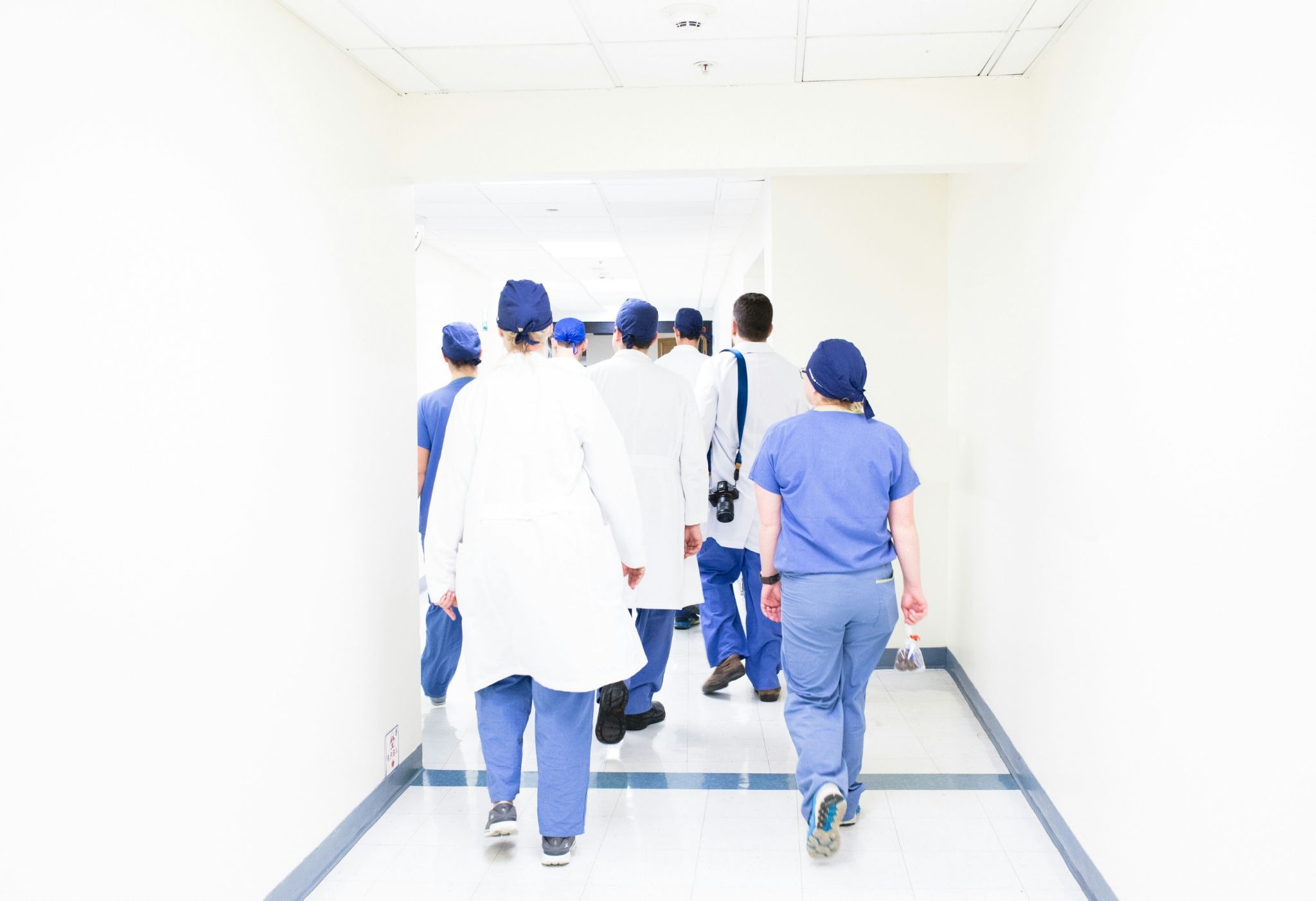 Group of healthcare professionals and doctors in blue scrubs and lab coats walking down a bright hospital corridor